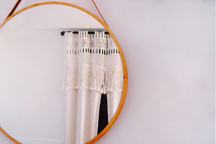 A round wall mirror showing curtains in the reflection