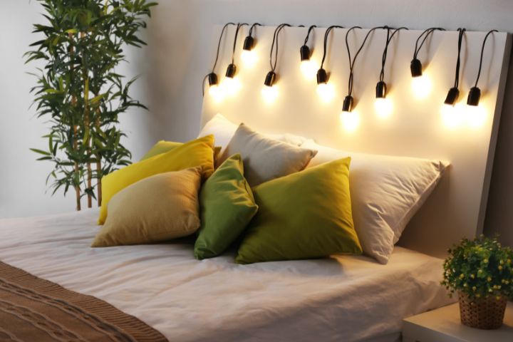 Bed with hanging lighting and plants and decorative green cushions