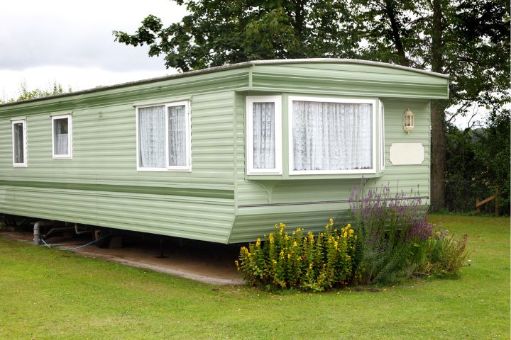 Green static caravan on grass with flowers in front