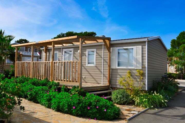 Static caravan with a wooden balcony and greenery out front